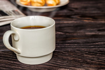 White cup with coffee and croissants on a wooden background, selective focus. The concept of breakfast.