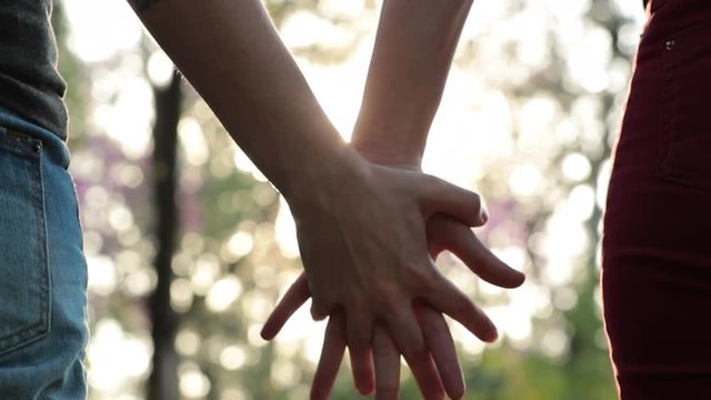 Close-up of couple holding hands together at the park with sunlight flare in the background
