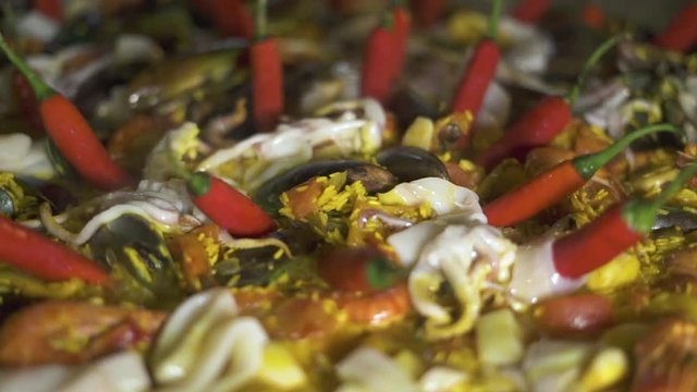 Traditional spain food paella with mussels, shrimps, calamari and vegetables in pan. Close up. Cooking spanish paella with red hot peppers and fresh seafood in pan close up.