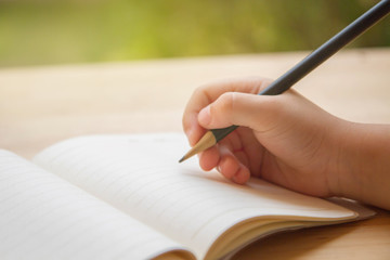 Kid hand holding black pencil and writing on blank book
