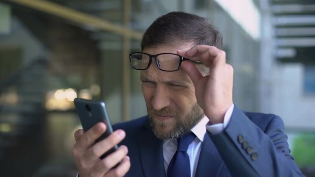 Manager in eyeglasses trying read smartphone message, poor eyesight, health care