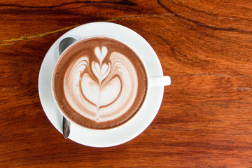 coffee cup latte art on wooden table.hot drink coffee with milk froth for breakfast.heart shape art foam texture top view.
