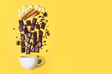 Rolgordijnen Chocolade Warme chocoladekop, chocoladestukjes, kruiden en marshmallows op gele achtergrond