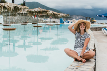 beautiful happy young woman in straw hat sitting near pool and smiling at camera, montenegro