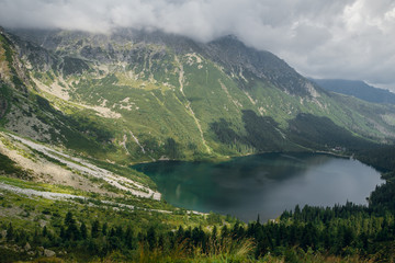 Top view shot of beautiful green hills and mountains in dark clouds and reflection on the lake Morskie Oko lake, High Tatras, Zakopane, Poland. Sunny day
