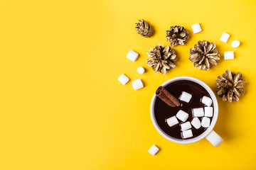 Hot chocolate cup with cinnamon and marshmallow on yellow background. Warming Christmas winter drink