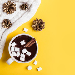 Hot chocolate cup with cinnamon and marshmallow on yellow background. Warming Christmas winter drink