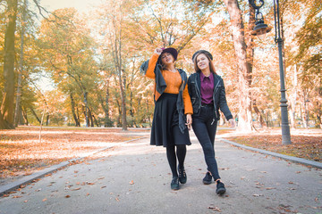 Two teenage girls are having fun in the park, autumn outfit. Funny girl friends throwing dry leaves in the city in autumn. Happy family on autumn walk!