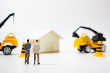 Miniature businessman in miniature house construction site.