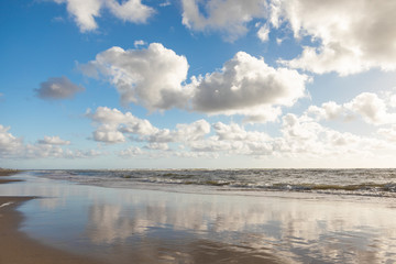 Bank of the blue sea with wet sand and clouds