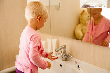 Happy boy washes his hands with soap and brushes his teeth in bathroom. Child loves water and hygiene procedures. Water activities for children. Hygiene and skin care for children. Bathroom interior