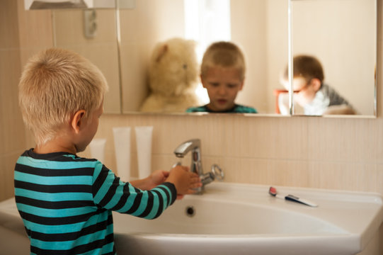 Happy boy washes his hands with soap and brushes his teeth in bathroom. Child loves water and hygiene procedures. Water activities for children. Hygiene and skin care for children. Bathroom interior