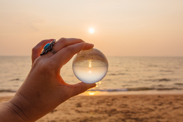 Lens ball in hand with reflection of sea and sunset on the beach