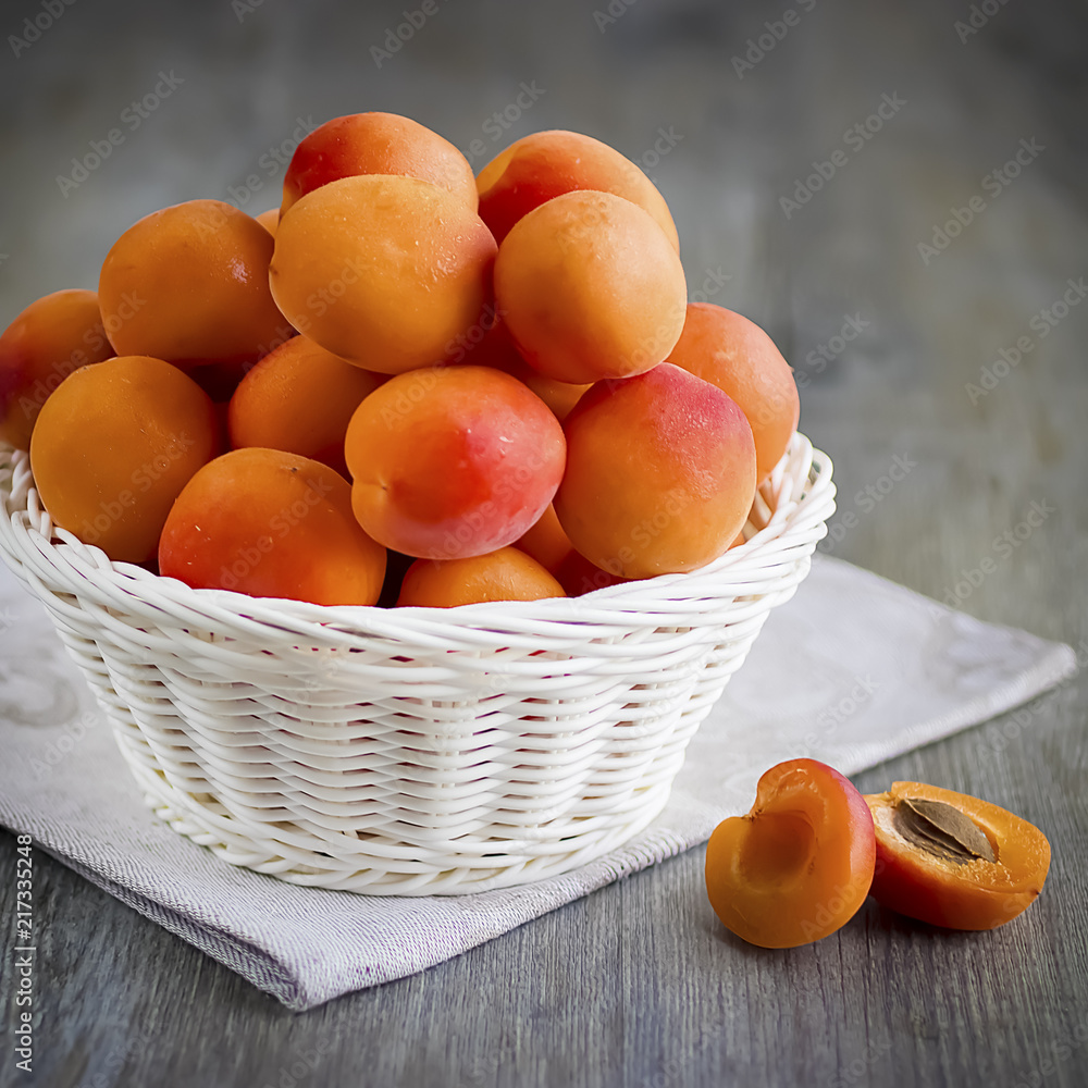 Wall mural ripe bright apricots in white basket, knife and gray napkin on wooden gray table.