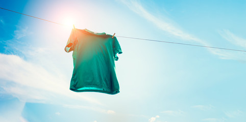 Green t-shirt on clothes line against sun and blue sky with clouds.