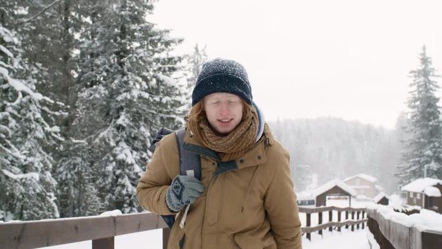 Young caucasian guy with backpack walking in national park at snowy day while traveling alone on winter vacation