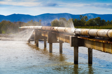 A leaking pipeline in the sun crossing a canal.