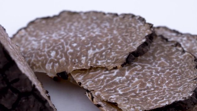 Super macro of black truffle slices slowly rotating on the on the turntable. Isolated on the white background. Closeup.