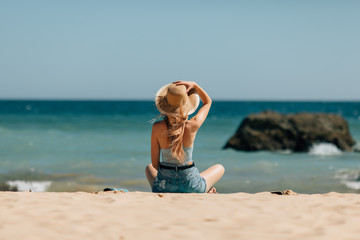 Fototapeta na wymiar Rear view of woman in straw hat relaxing on sandy beach view on ocean