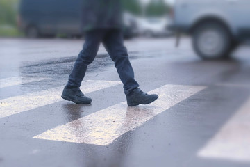 Boy crosses the road at a pedestrian crossing in the rain. Legs close-up.