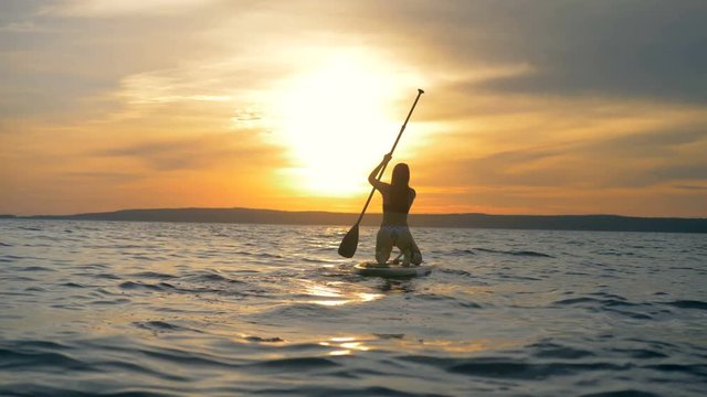 Sportswoman floats on a special board with a paddle on a sunset background. 4K.