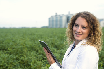 Smart agriculture. Scientist agronomist holding tablet in the green soybean field with silos.  © littlewolf1989