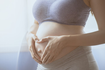 Young Pregnant Asian Woman Holds Her Hands on Her Swollen Belly, Love Concept.