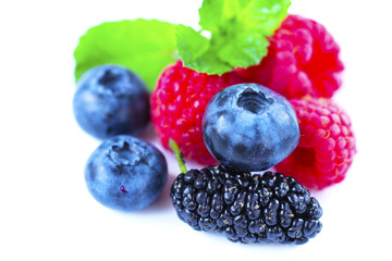 Close-up arrangement mixed, assorted berries including blackberries, strawberry, blueberry, raspberries and fresh leaf on white