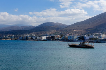 a small village on the shores of the Mediterranean Sea; mountains are visible in the background, with sea by boat in the foreground; Sea view with mountains and blue sky with white clouds