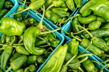 Organic green jalapeno peppers in blue paper boxes at a farmer's market. Boxes are oriented diagonally in photo.