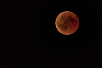 a full moon or blood moon during a complete lunar eclipse in a black night sky with stars