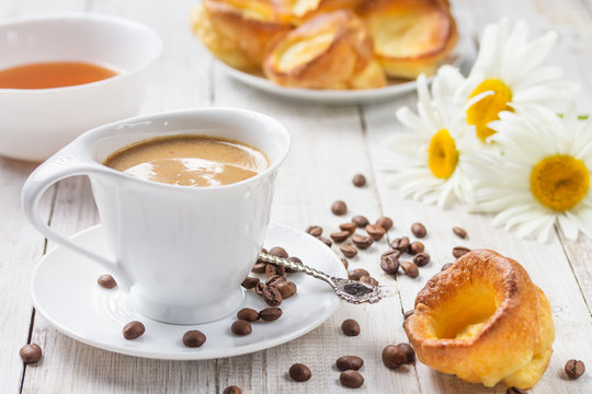 A cup of hot coffee with yorkshire puddings and haney, and daisies on a white wooden table. Breakfast