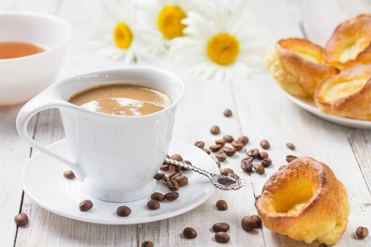 A cup of hot coffee with yorkshire puddings and daisies on a white wooden table. Breakfast