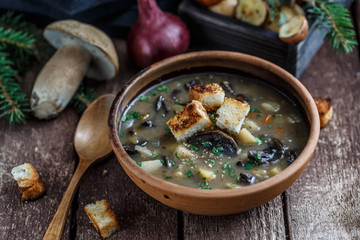 Mushroom soup in ceramic bowl with a copper pan and mushroom in background, dark photo.