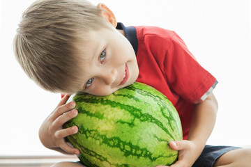 Fototapeta premium A cute boy and a big green watermelon. The child smiles and rejoices.