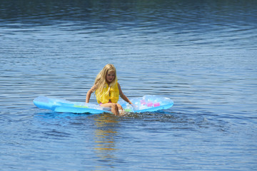 Beautiful young girl wearing a lifejacket and sitting on inflatable mattress on sea water