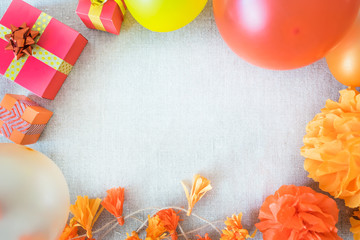 Birthday party background with festive decor, orange, yellow and red ribbons, gift boxes, balloons, garland, pompoms on neutral fabric. Colorful celebration background, copy space, Flat lay, top view.