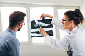 Obraz premium Portrait of Woman Doctor at her Medical Office Looking at X-Ray with Patient