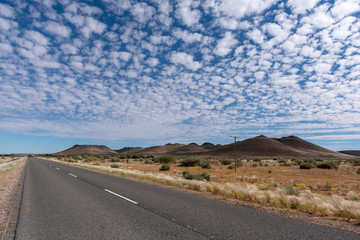 Straight road leading to horizon and beautiful scattered white clouds in blue sky
