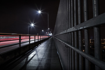 The Second Narrows Bridge sidewalk at night, with light trails from passing cars.