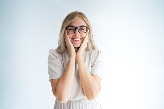 Amazed happy blonde girl surprised with good news. Beautiful young Caucasian woman in glasses touching cheeks and broadly smiling. Promotion concept