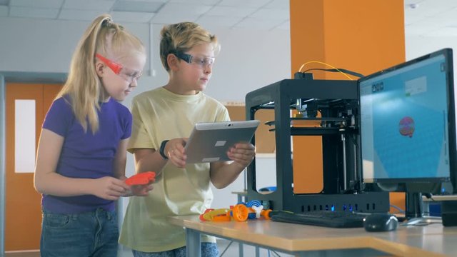 A boy and a girl work in a laboratory inventing 3d printed robot.
