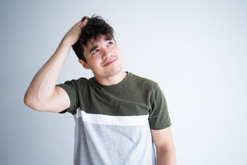 Pensive smiling curly guy scratching head and looking up. Young mixed race man thinking over decision and trying to make right choice. Decision making concept