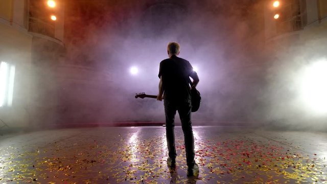 Concert rock band performing on stage with singer guitar. Music video punk, heavy metal or rock group. The guitarist performs on stage. Stage light, smoke. Back view