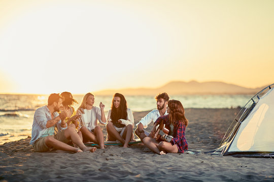 Friends with guitar at beach enjoyment. friends relaxing on sand at beach with guitar and singing on summer sunset.