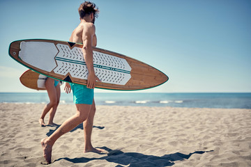 Naklejka na ściany i meble Healthy Active Lifestyle. Surfing. Summer Vacation. Extreme Sport. Young surfer man walking with board on the sandy beach. .