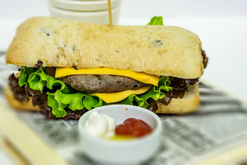 Close up of a fresh burger with home-made bread with spices and olives, red and green salad and a bowl of sauces, ketchup, mustard and mayonnaise. Shallow depth of focus.