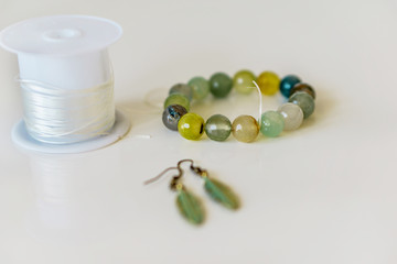 Close-up of handmade jewelery, bracelet of multicolored agate and feathers earrings, on a white background. Concept fashion and beauty.