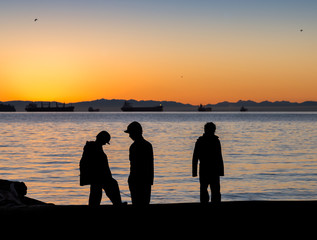 Three children looking out across the water towards the sunset.