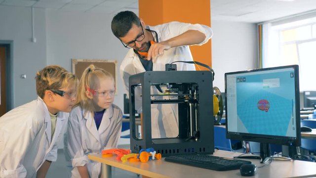 Children and a school teacher work with a 3D printer in a laboratory, close up.